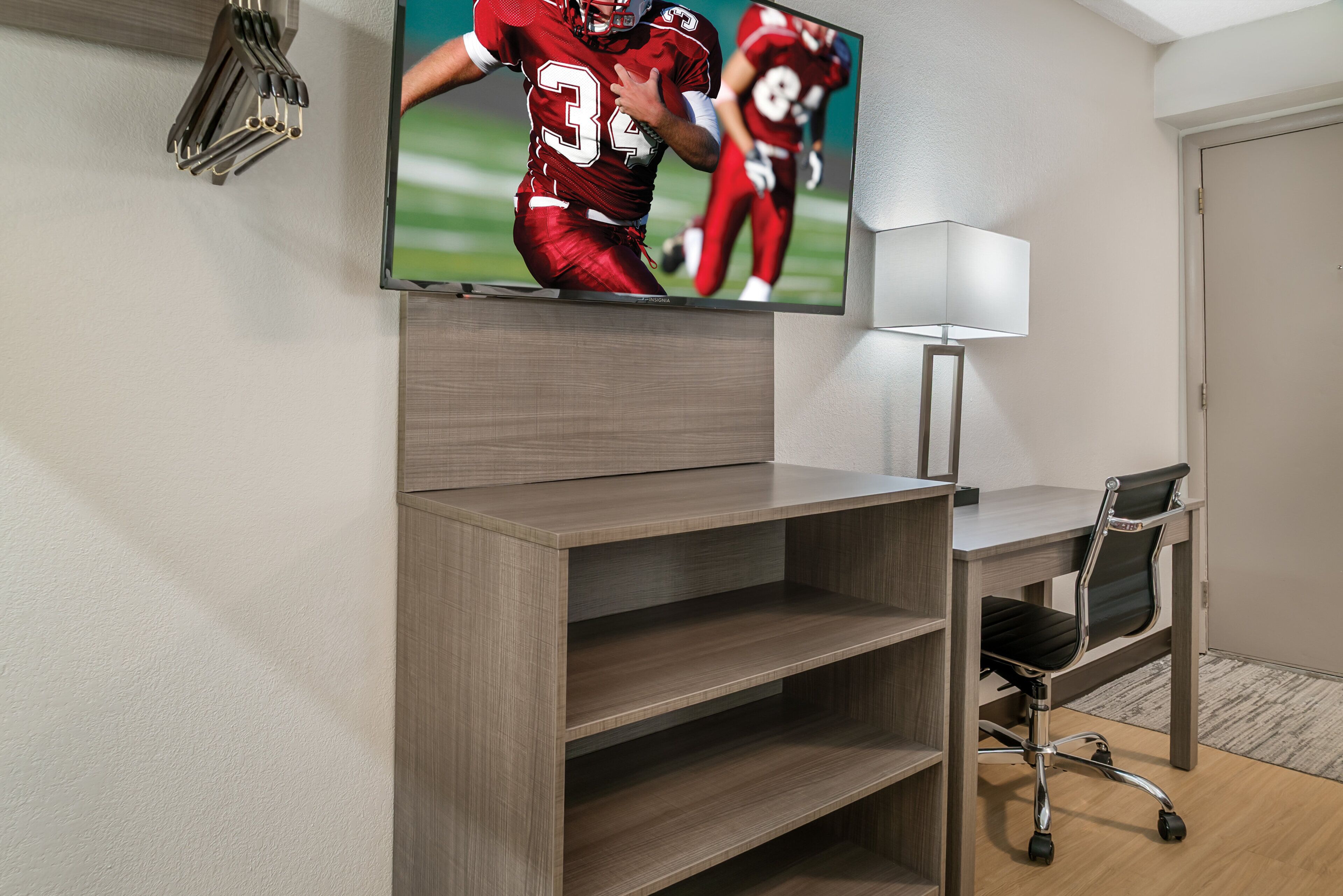 Une pièce avec un téléviseur fixé au mur, un bureau avec une chaise et une lampe.