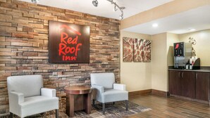 A Red Roof Inn reception area with a stone wall, two armchairs, a small table, and a coffee machine. - Red Roof Inn Detroit Metro Airport - Taylor (Taylor)