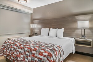 Habitación de hotel con una cama grande, una mesita de noche con lámpara y un televisor montado en la pared.