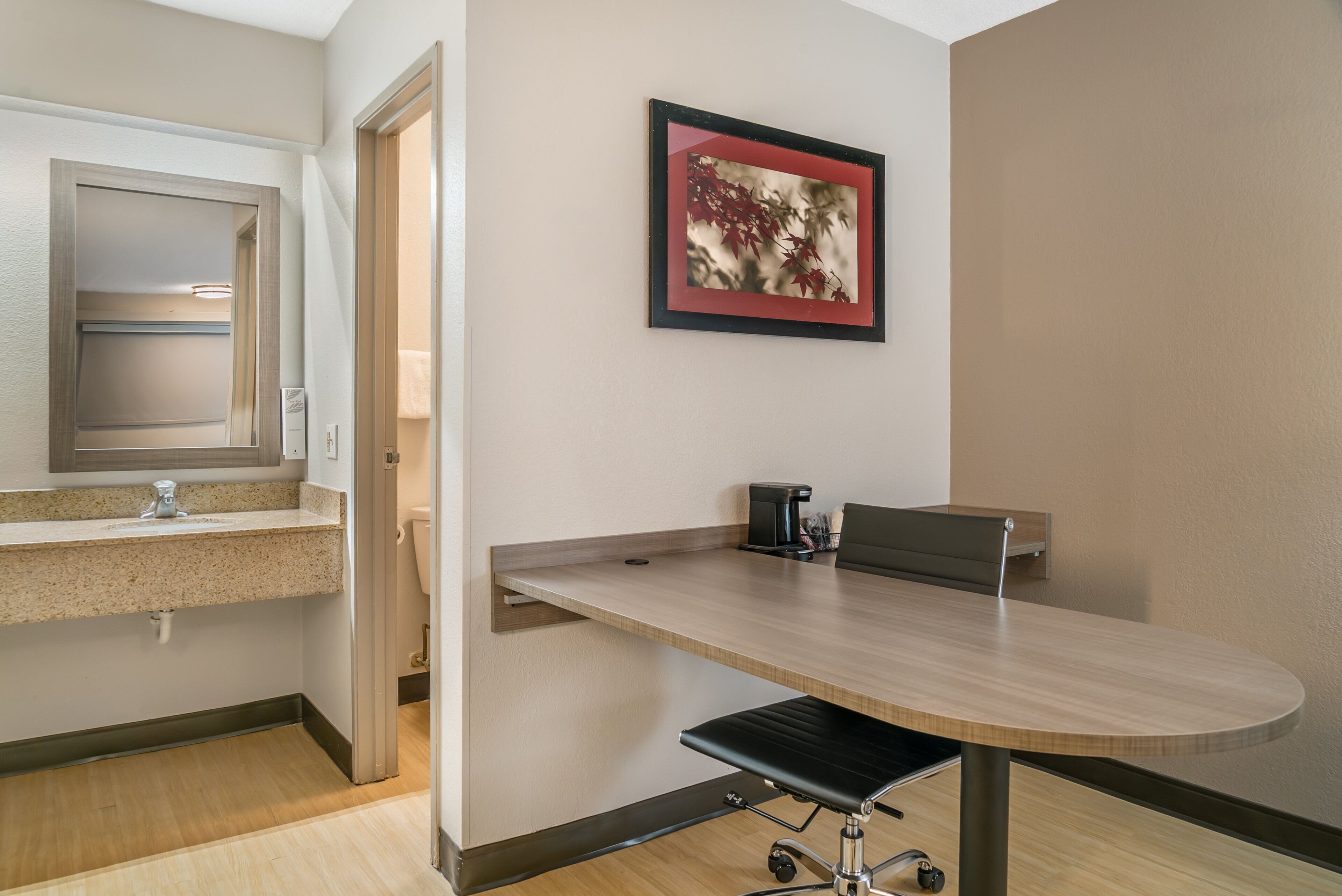 A modern hotel room with a kitchenette, a dining table, and a framed picture on the wall.
