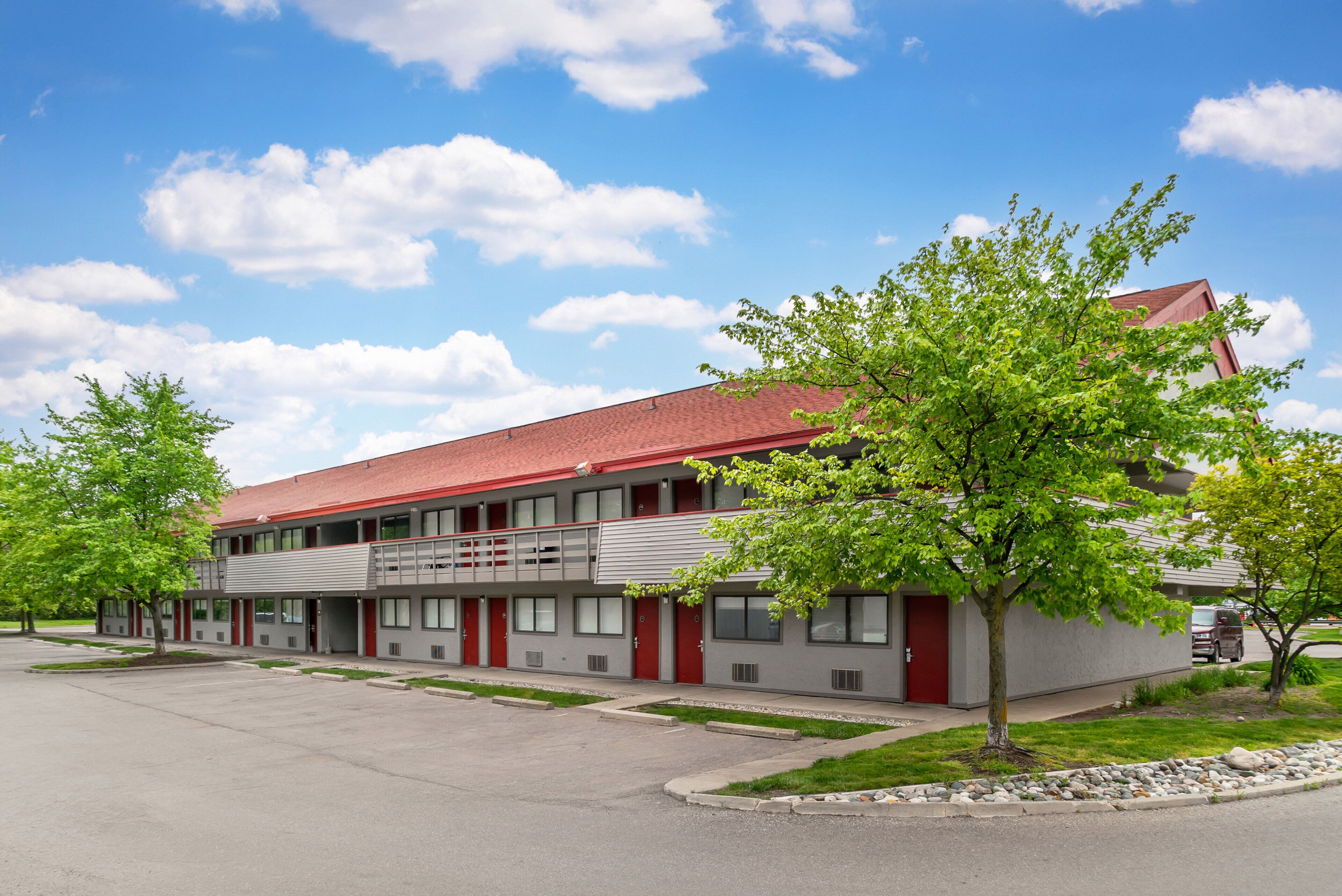A two-story motel with a red roof, multiple windows, and a parking lot.