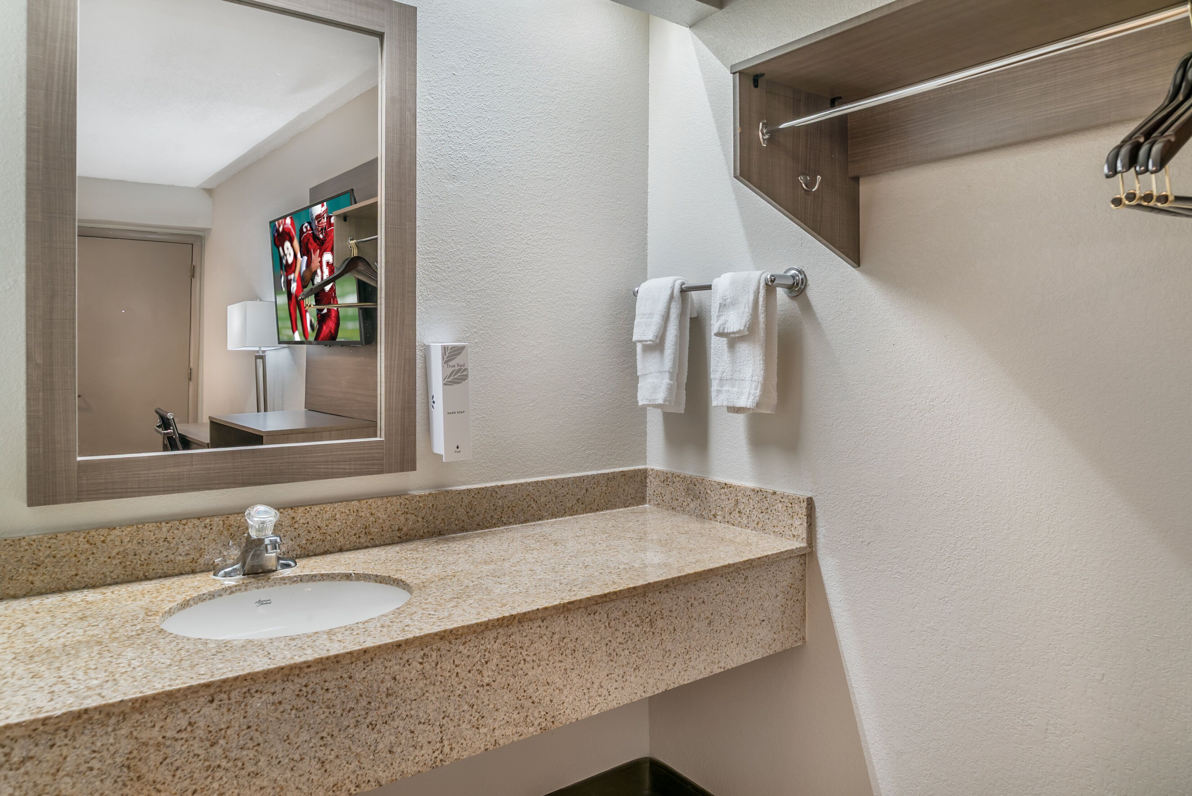 A bathroom with a granite countertop sink, a mirror, a towel rack, and a towel dispenser.