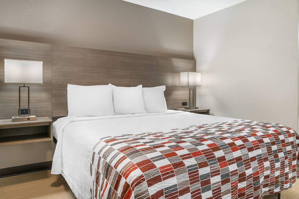 A hotel room with a large bed, two bedside tables, a nightstand, a wall-mounted lamp, and a bedside table lamp.