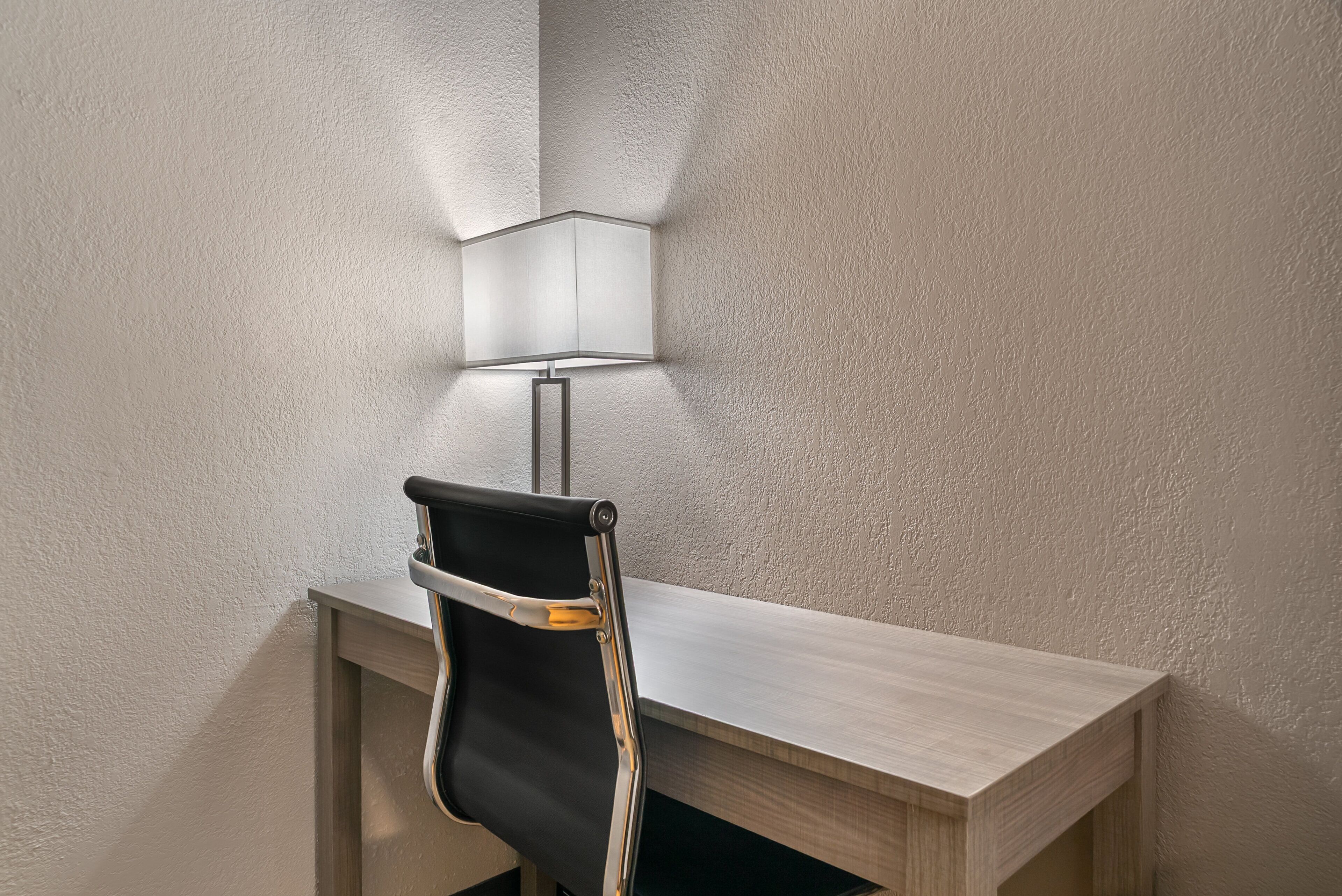 Een hoekbureau met een moderne lamp en een zwarte stoel.