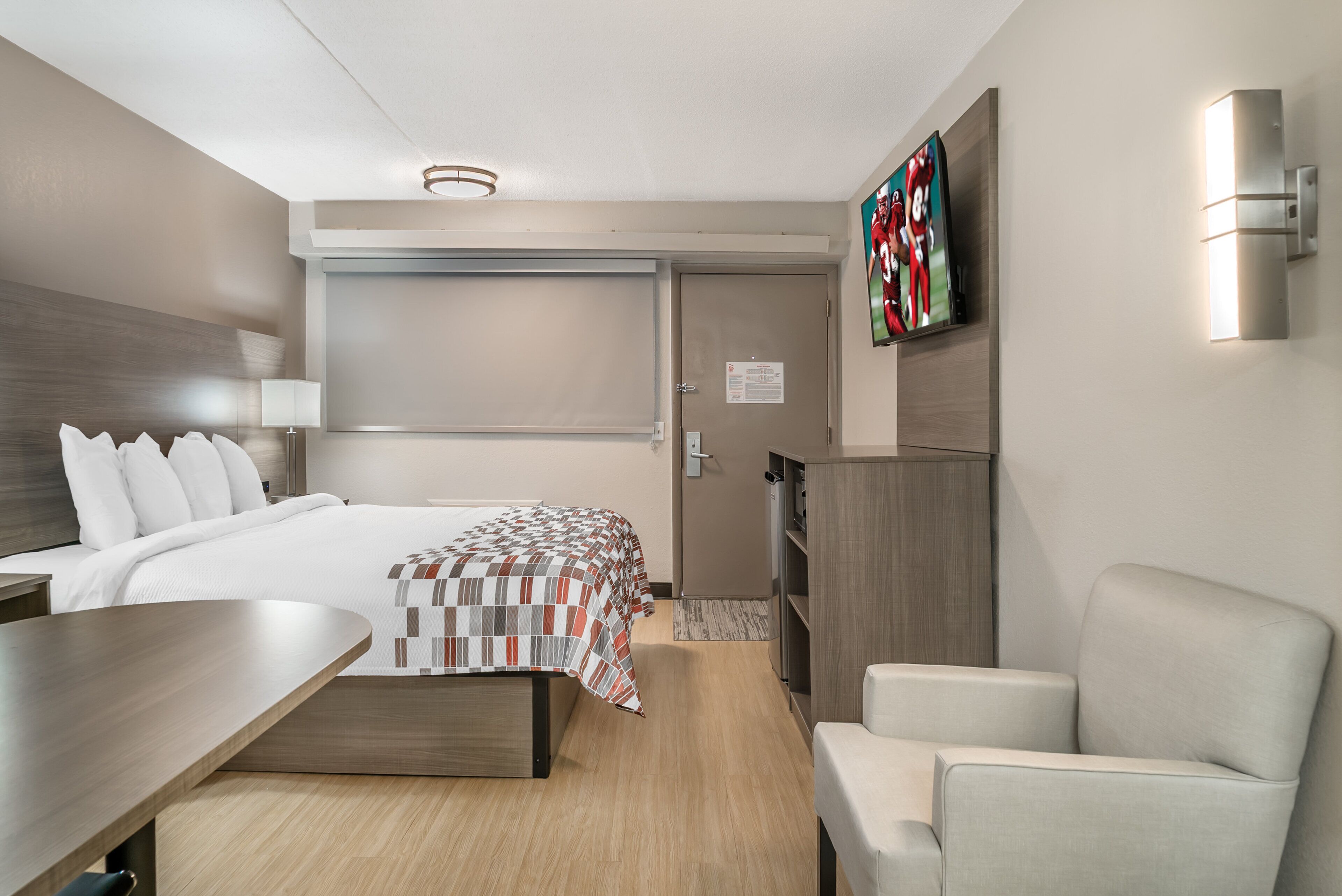 A modern hotel room with a bed, a desk, a chair, a TV, and a wardrobe.