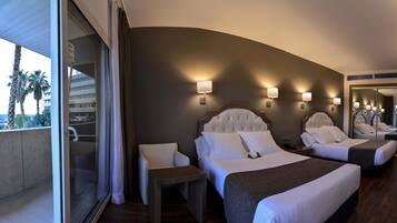Una habitación de hotel con una cama grande, un área de descanso y vistas a palmeras.