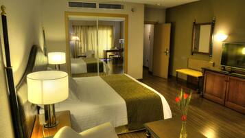 A hotel room with a bed, bedside table, lamp, mirror, dresser, and a vase with flowers.