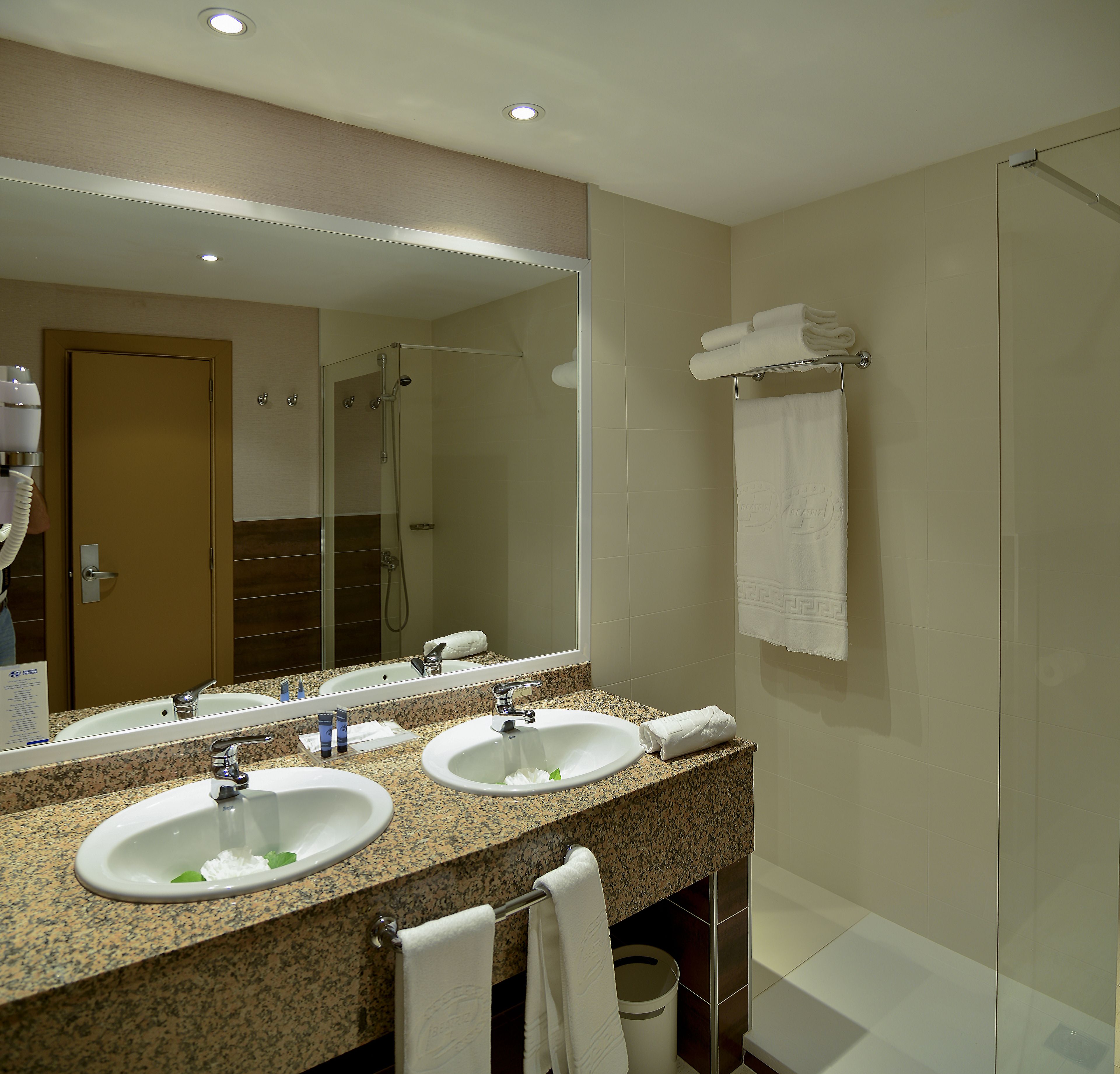 A bathroom with two sinks, a large mirror, a shower, and a towel rack.