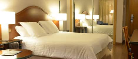 Una habitación de hotel con cama, mesitas de noche, una silla y un espejo.