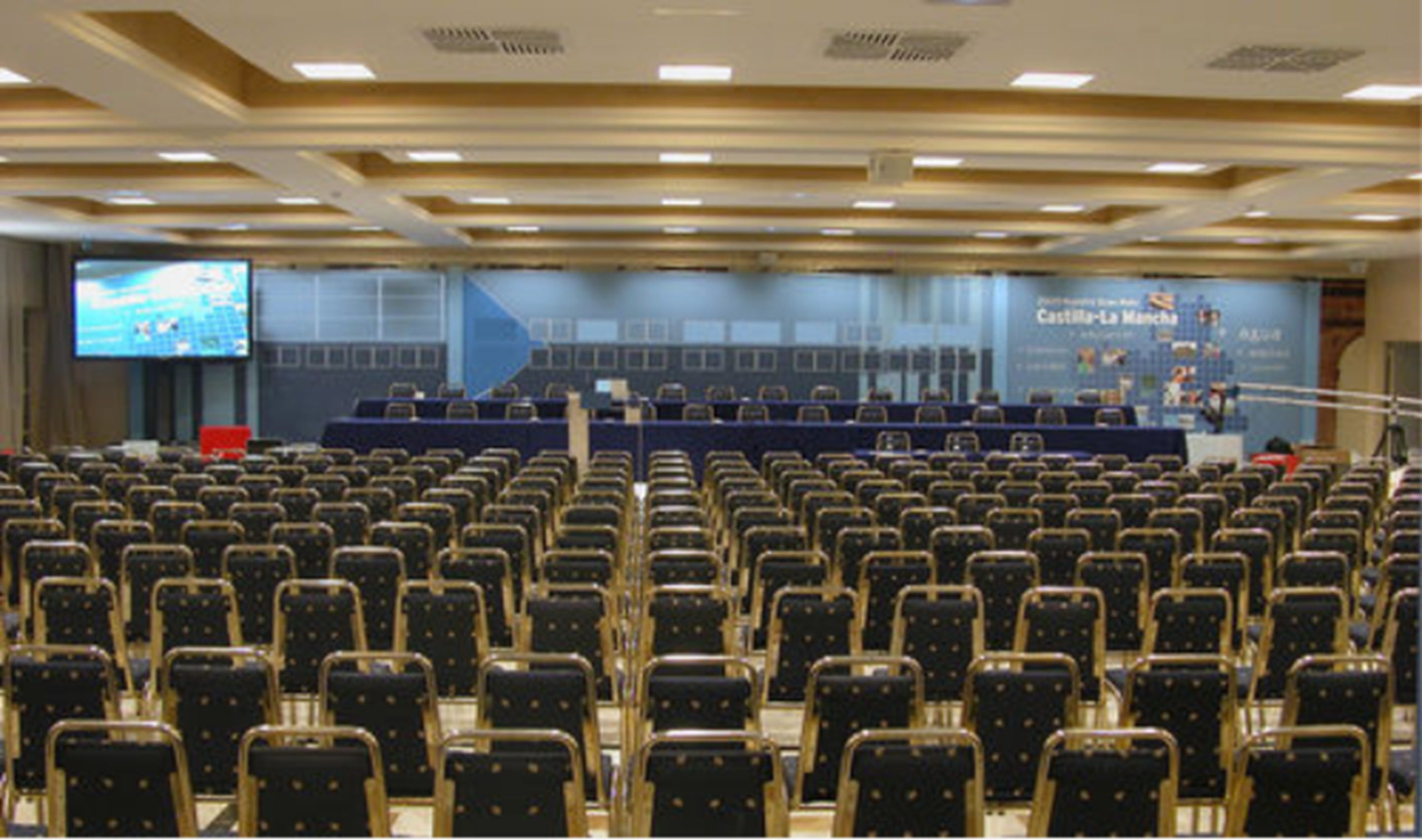 A conference room with rows of chairs, a large screen, and a stage with a podium.
