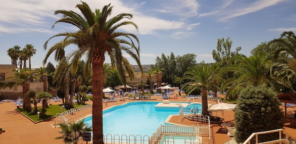 Un área de piscina con palmeras, sillas de descanso y sombrillas.