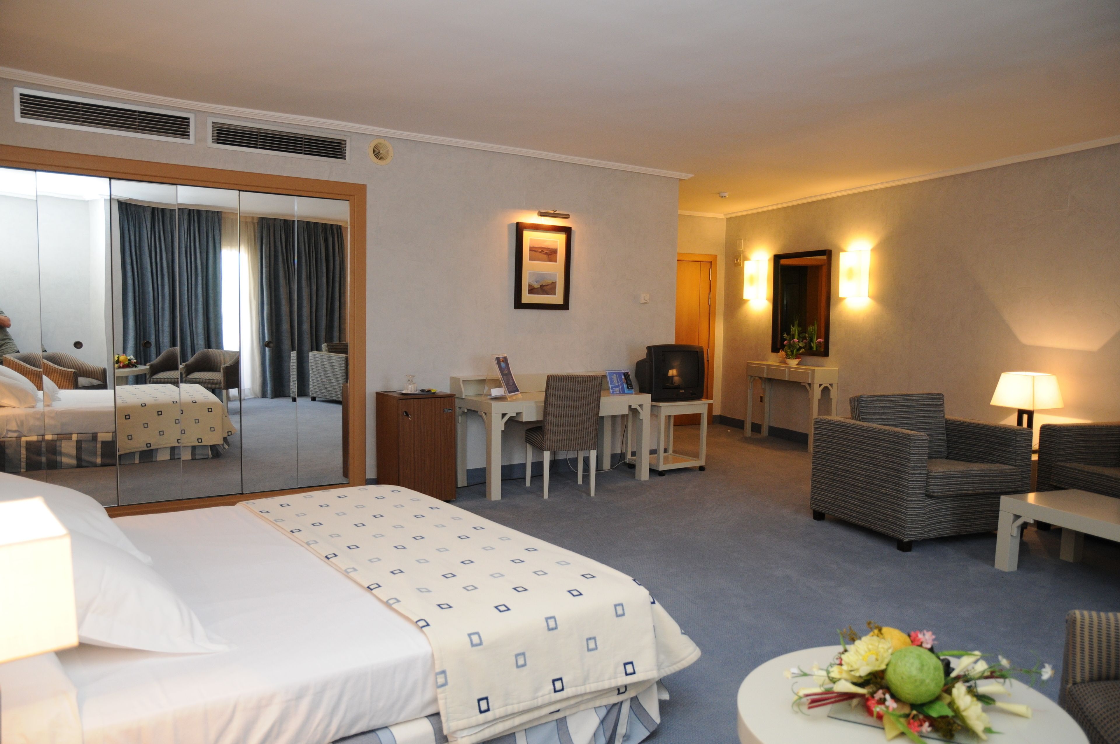 Et hotelværelse med seng, skrivebord, stol, sofa og spisebord med blomster.
