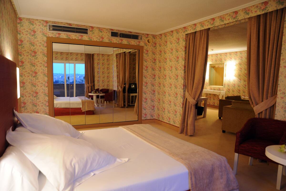 A hotel room with a bed, a desk, a chair, and a bathroom visible through a mirror.