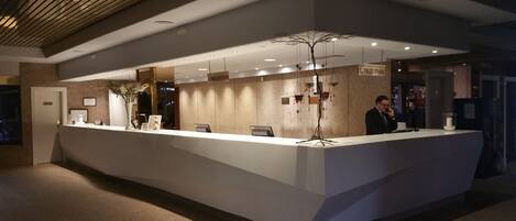 A reception desk with a modern design, a sign indicating the reception area, and a decorative tree-like structure above it.
