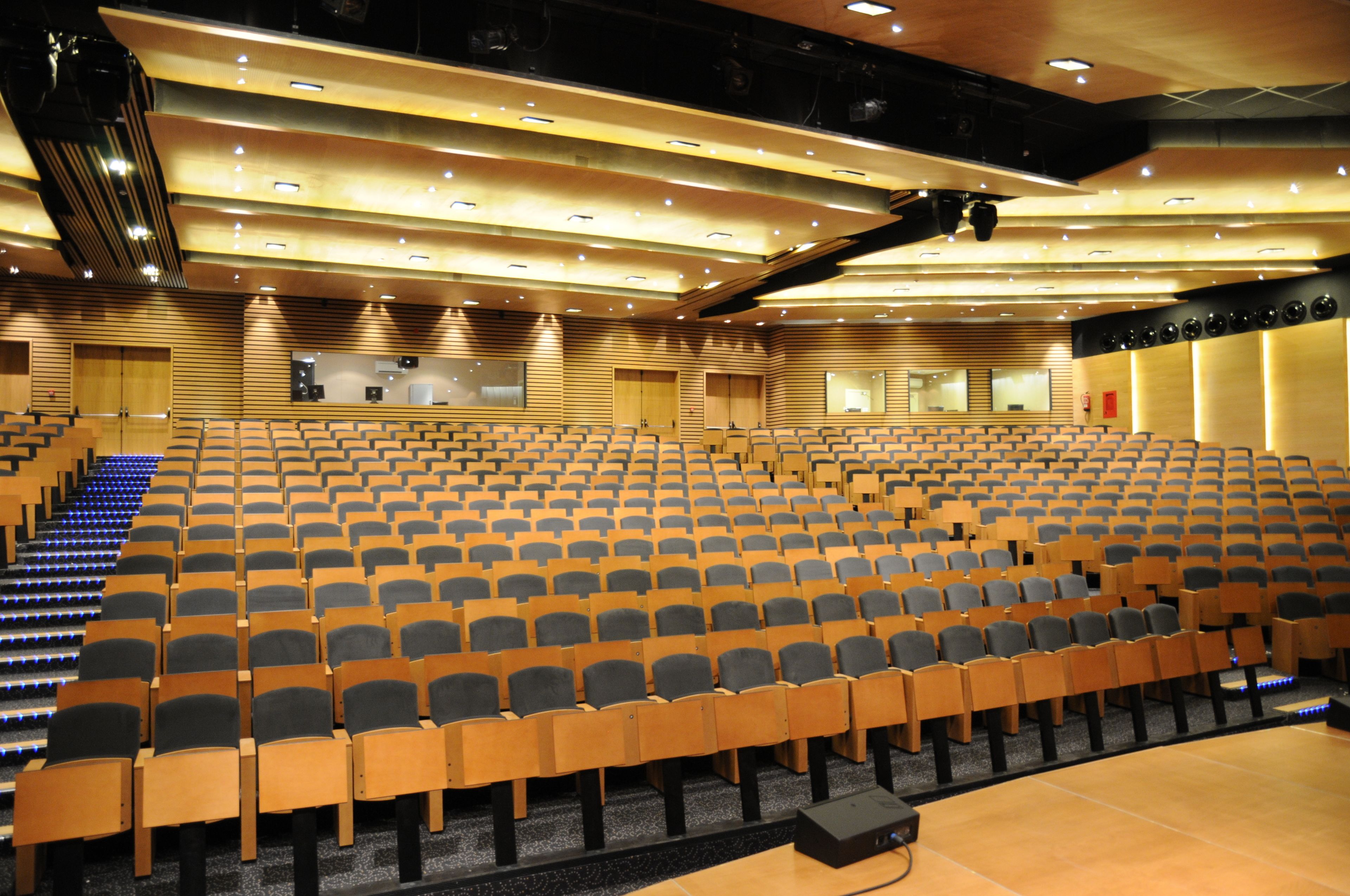An auditorium with rows of wooden chairs and a stage area.