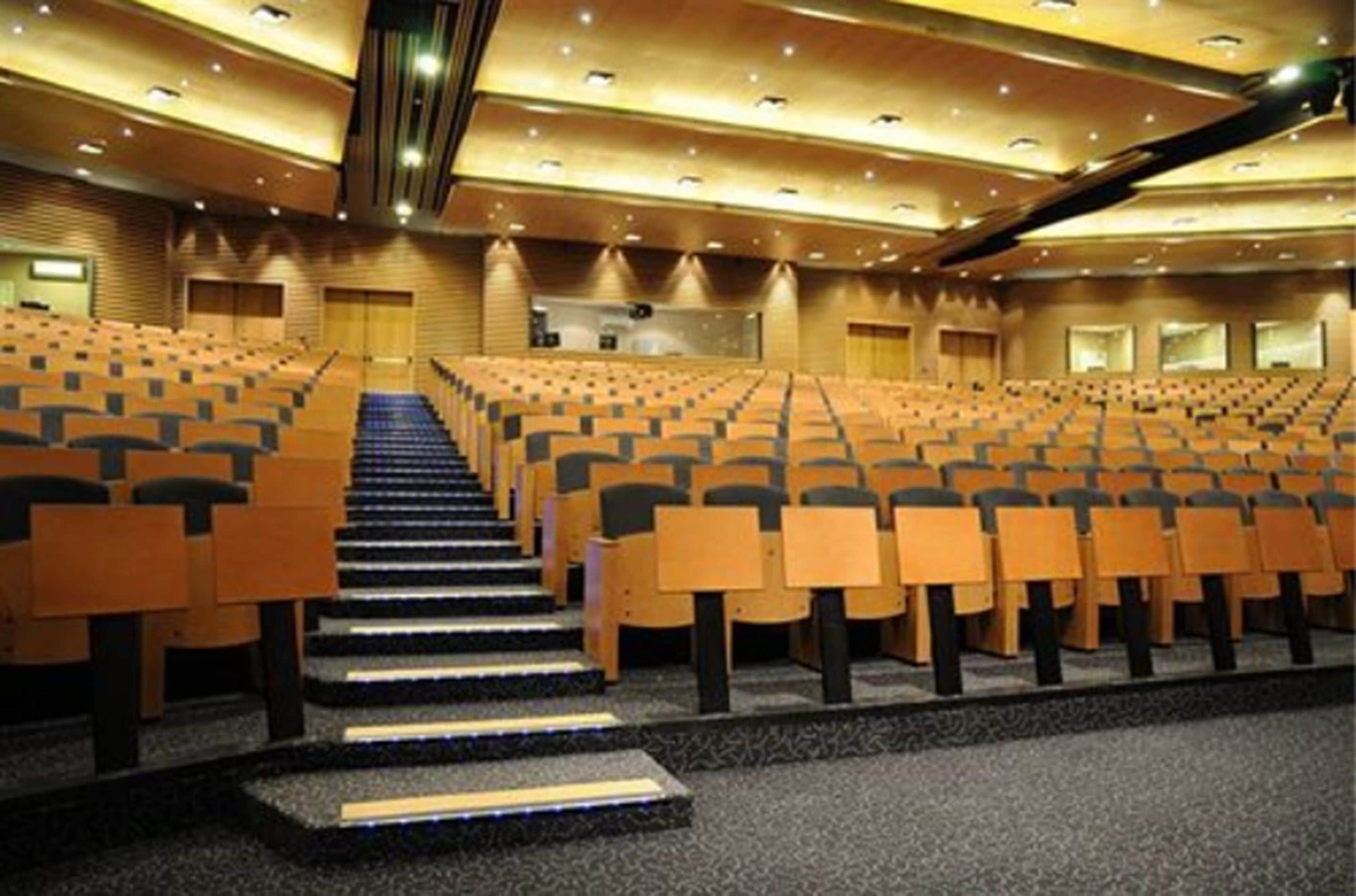Un amplio auditorio con asientos escalonados, un escenario central y un diseño moderno.