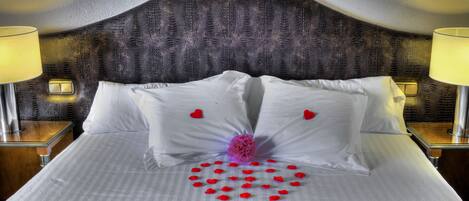 A neatly made bed with white linens, a decorative heart pattern on the bedspread, and two bedside lamps on wooden nightstands.