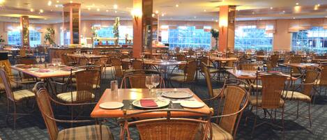 Un comedor amplio con varias mesas y sillas de mimbre, ventanas grandes y un ambiente cálido.