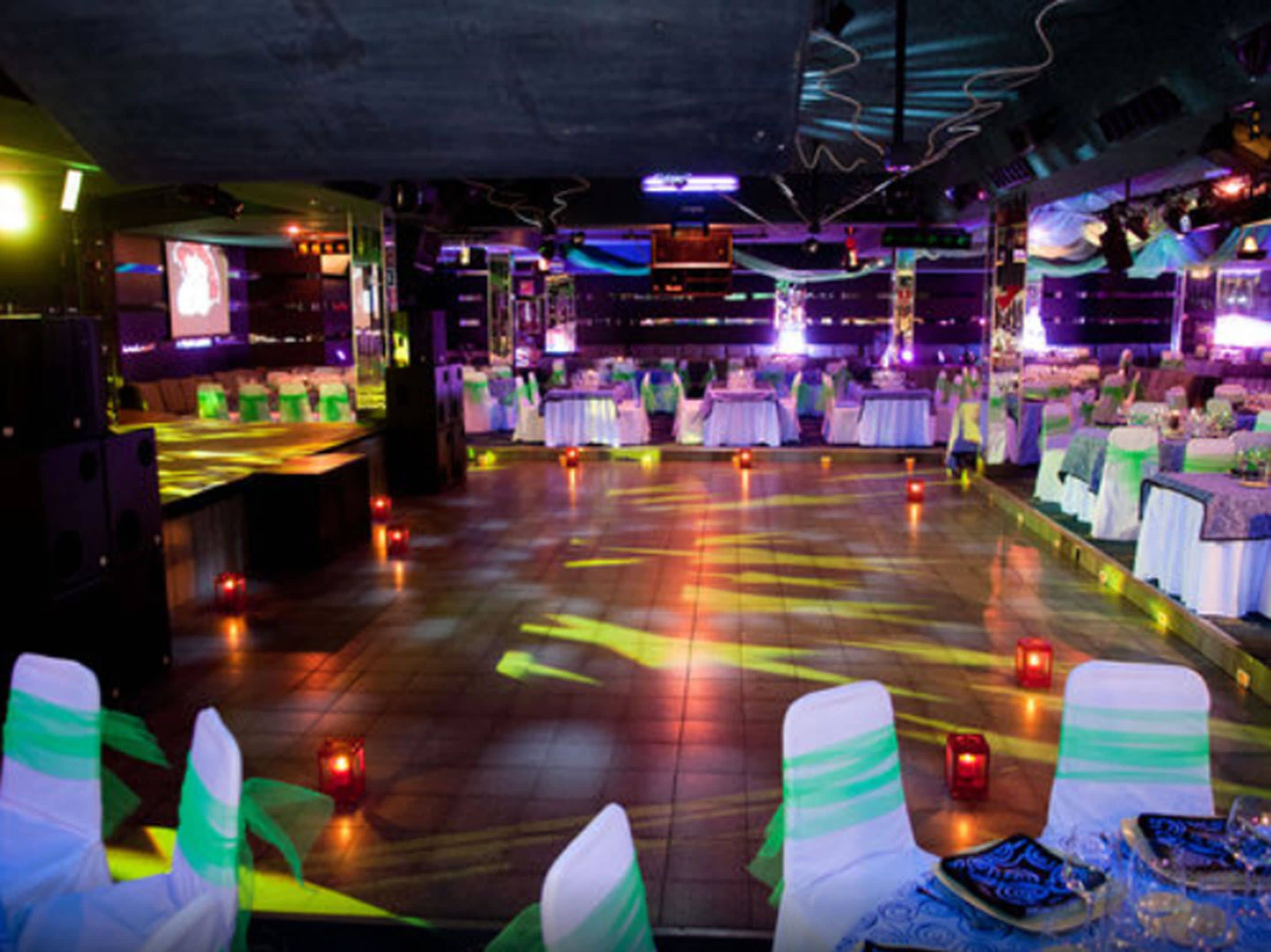 A spacious indoor venue with a dance floor, tables set for dining, and a stage area.