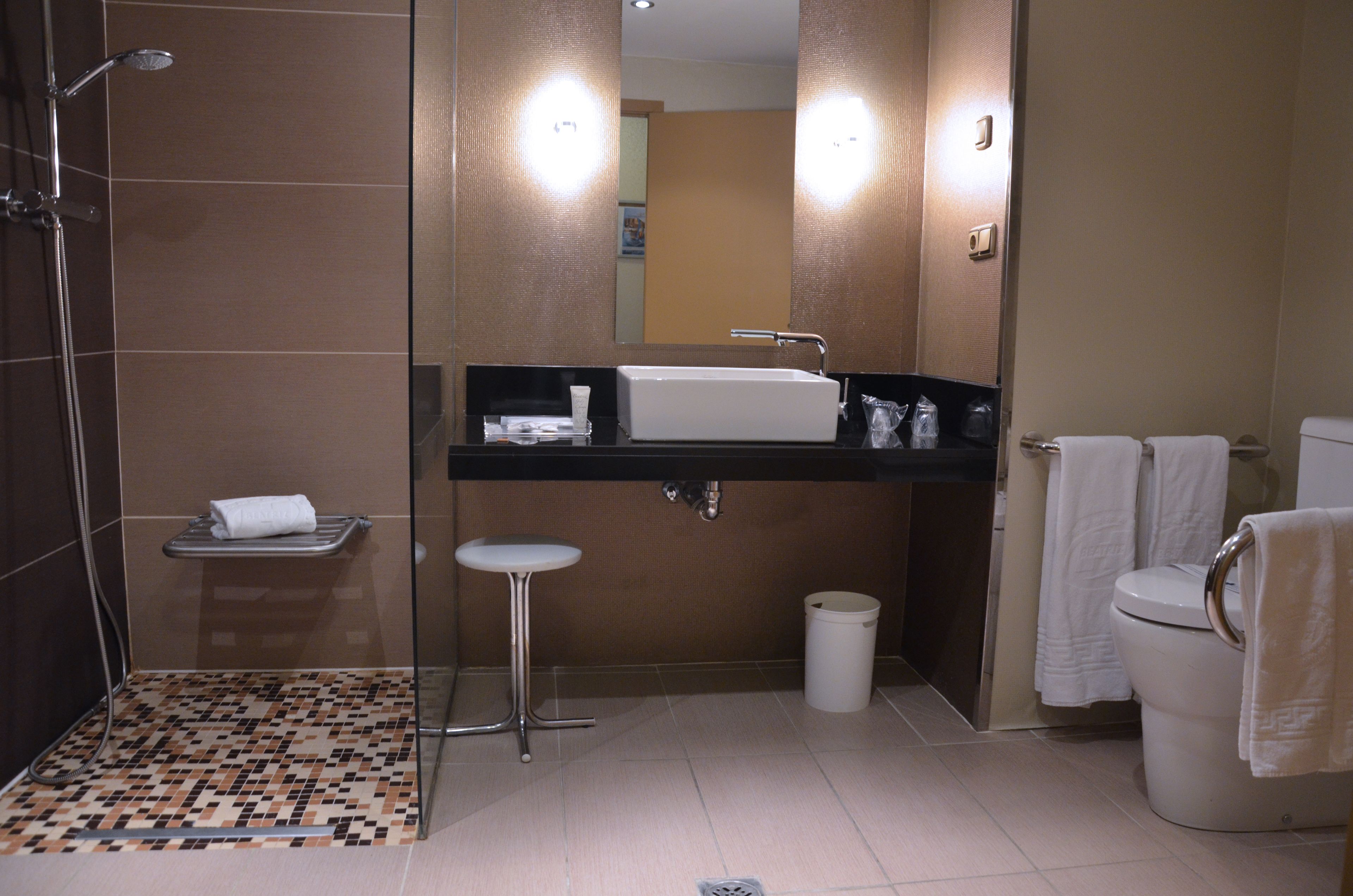 Un baño moderno con ducha, lavamanos, inodoro y un taburete pequeño.