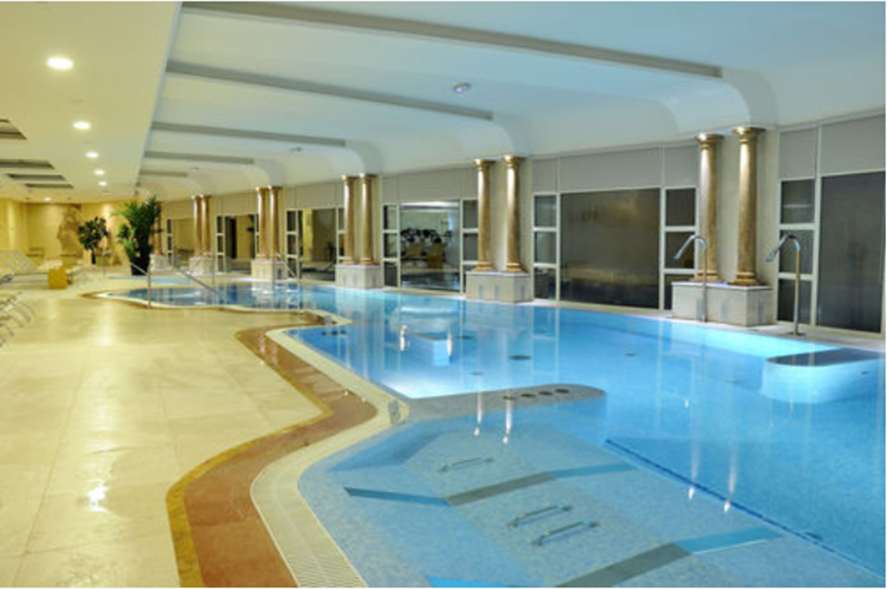 An indoor swimming pool with clear water, surrounded by columns and a tiled floor.