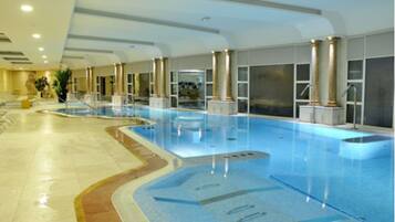 An indoor swimming pool with clear water, surrounded by columns and a tiled floor.