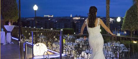 A woman in a white dress standing by a railing overlooking a cityscape at night.