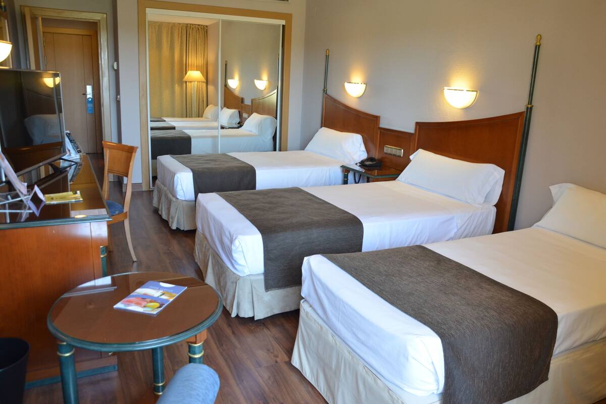 A hotel room with two single beds, a desk with a chair, a television, and a small table with a magazine.