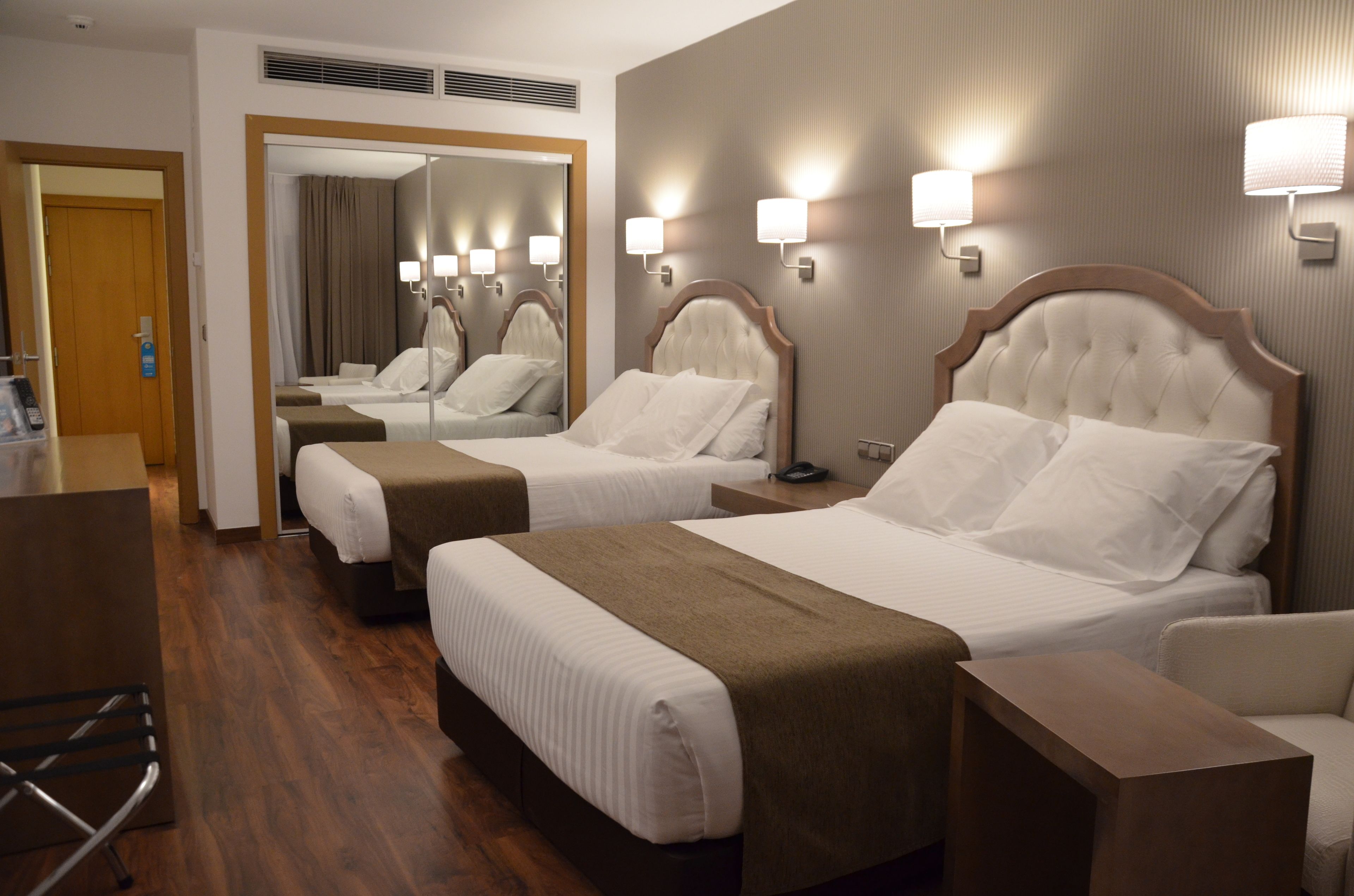 Una habitación de hotel con dos camas, un espejo, lámparas de noche y suelo de madera.
