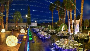 An outdoor dining area with string lights, palm trees, and tables set for a meal. - Hotel Beatriz Toledo Auditorium & Spa (Toledo)
