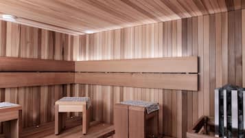 Un sauna avec des murs et des bancs en bois, un luminaire au plafond et une étagère en métal contenant des pierres.