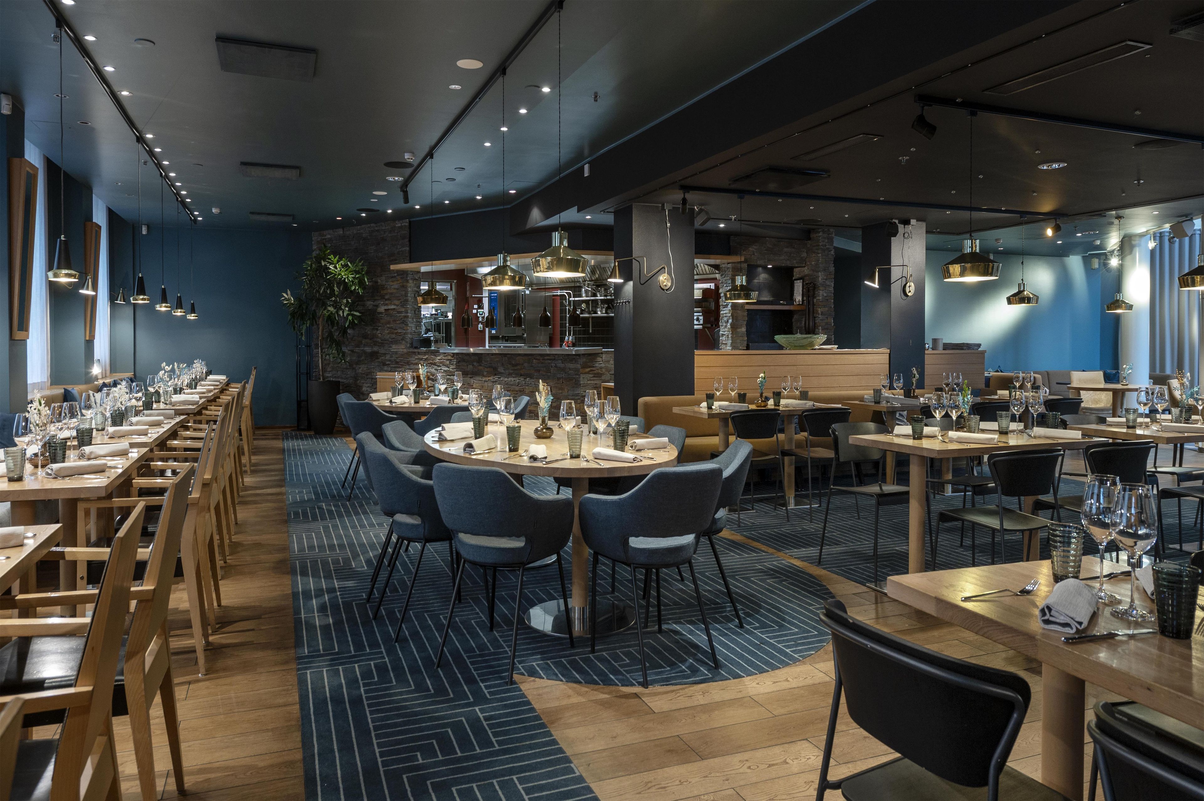 A restaurant with multiple dining tables and chairs, a bar area, and a kitchen in the background.