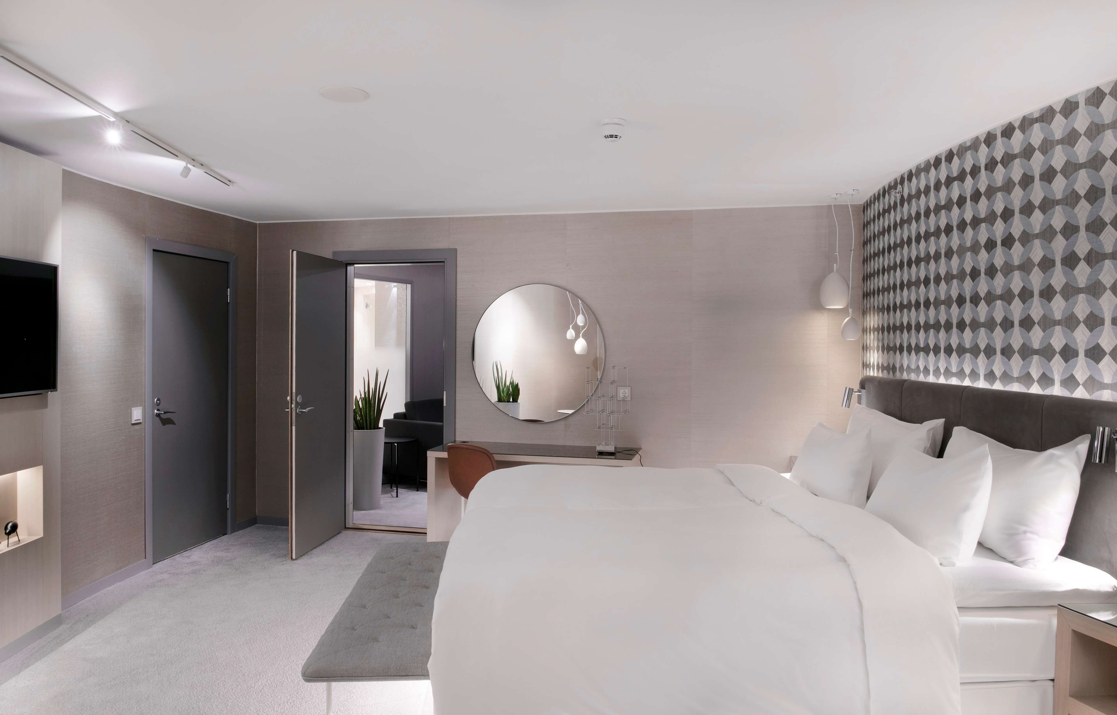 Una habitación de hotel moderna con una cama grande, un escritorio, un espejo y un televisor.