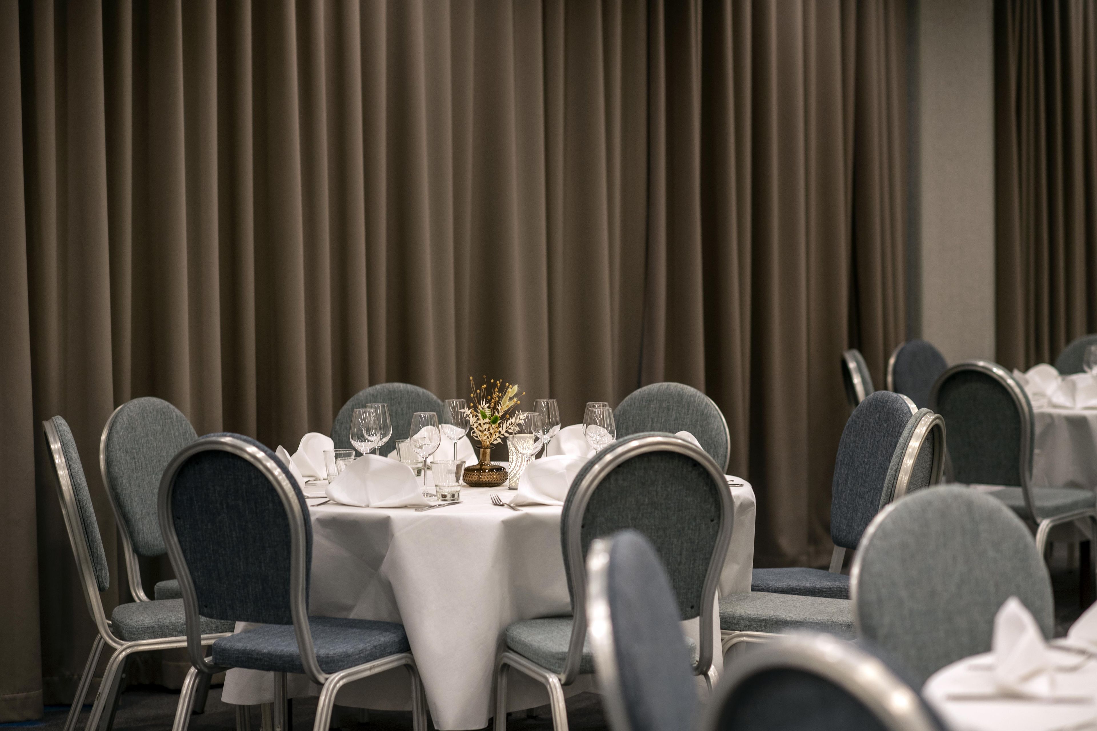A dining area with round tables set for a meal, chairs, and a curtain backdrop.