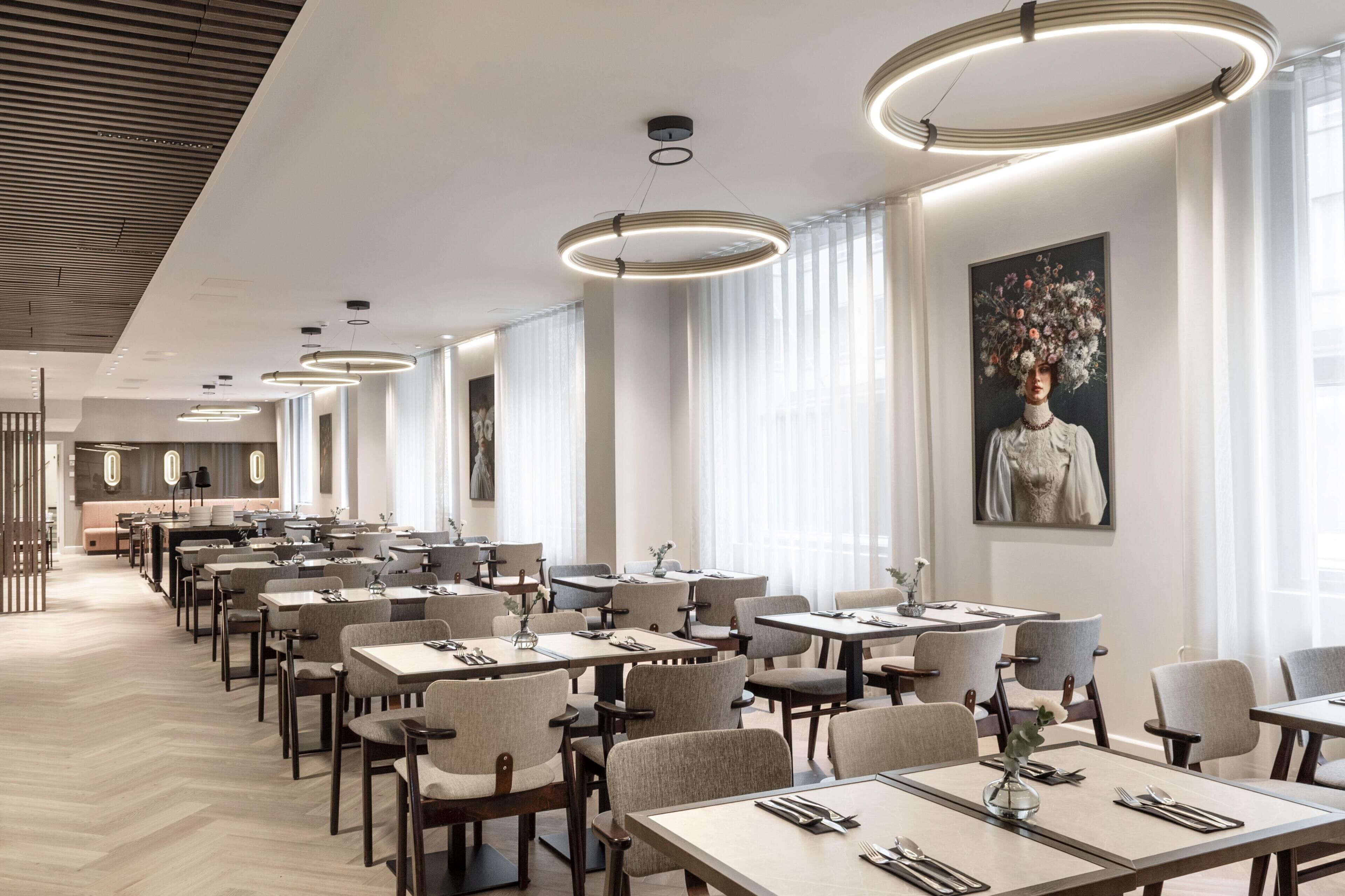 A modern restaurant with a long dining area, pendant lighting, and a large floral painting on the wall.
