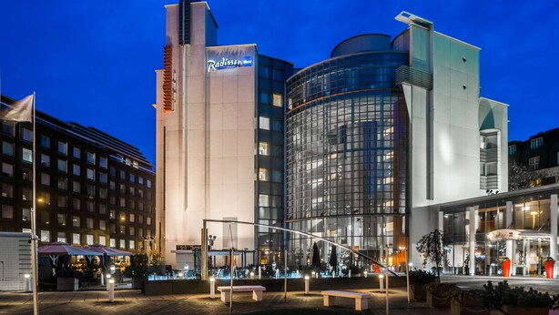 A Radisson hotel with a modern glass facade, a prominent vertical sign, and a well-lit outdoor area with seating. - Radisson Blu Royal Hotel Helsinki (Helsinki)