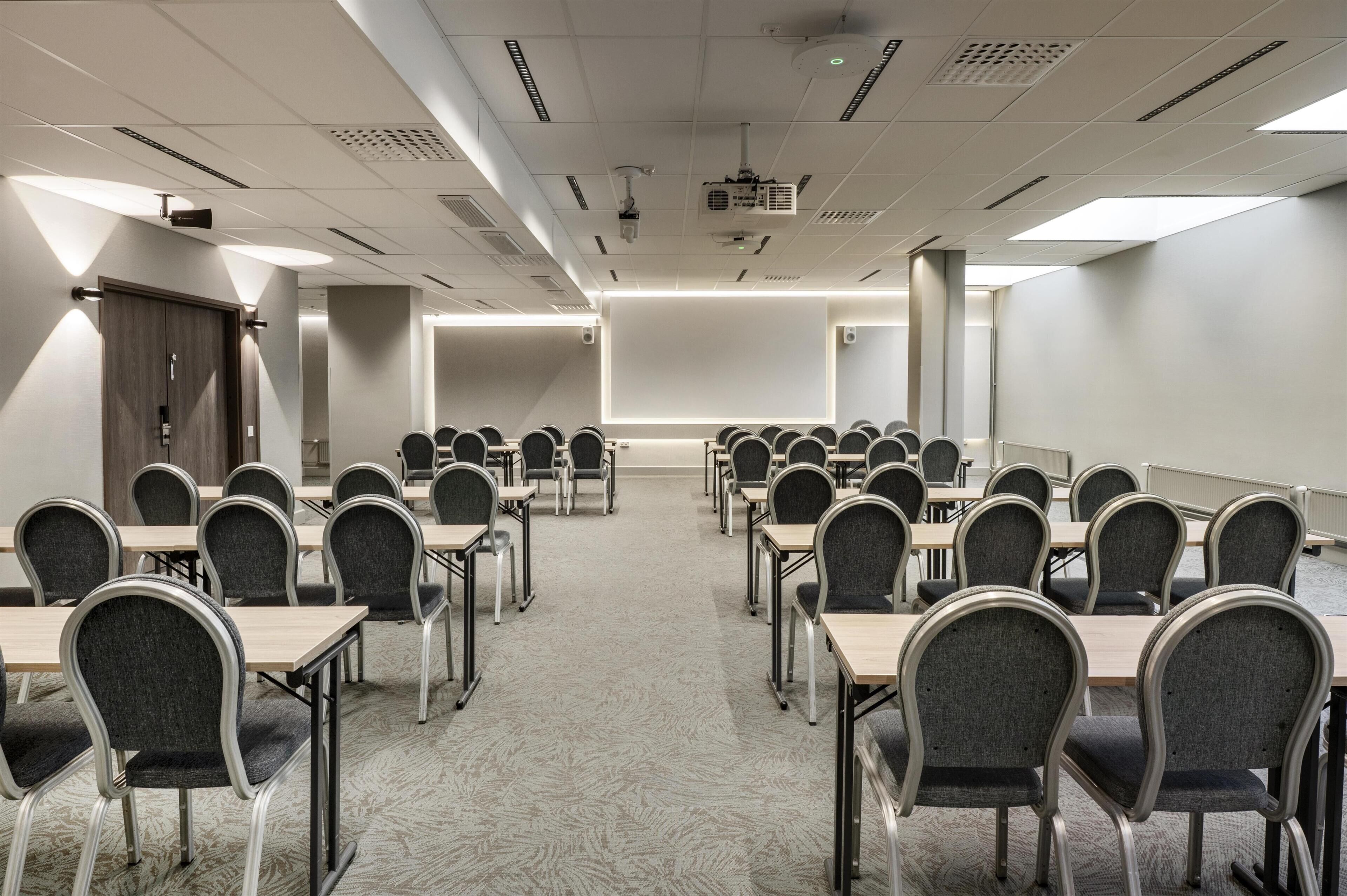 A conference room with rows of tables and chairs, a projector screen, and a whiteboard.