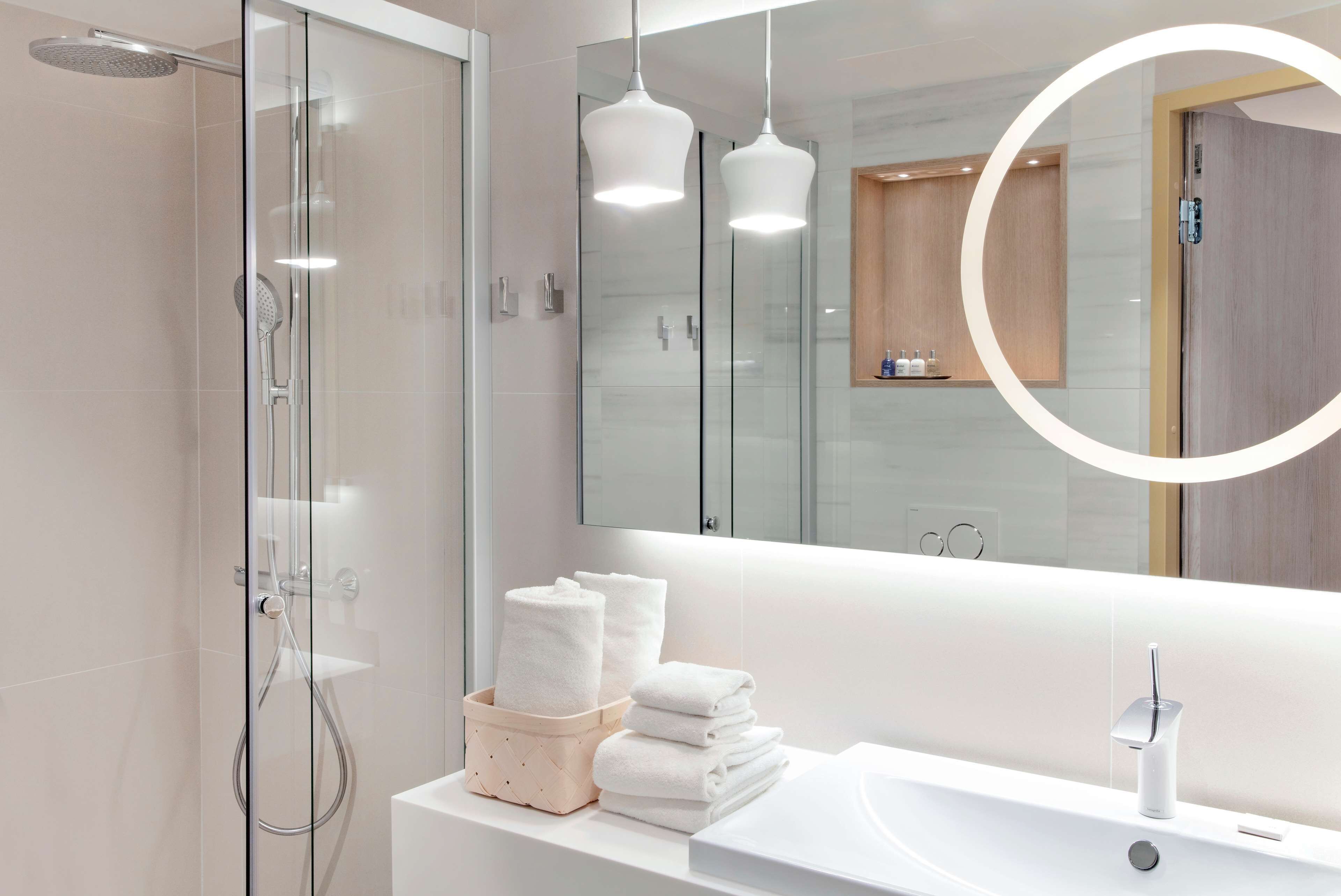 Un baño moderno con ducha envuelta en vidrio, un lavamanos blanco y un espejo grande.