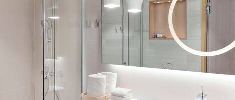 Un baño moderno con ducha envuelta en vidrio, un lavamanos blanco y un espejo grande.