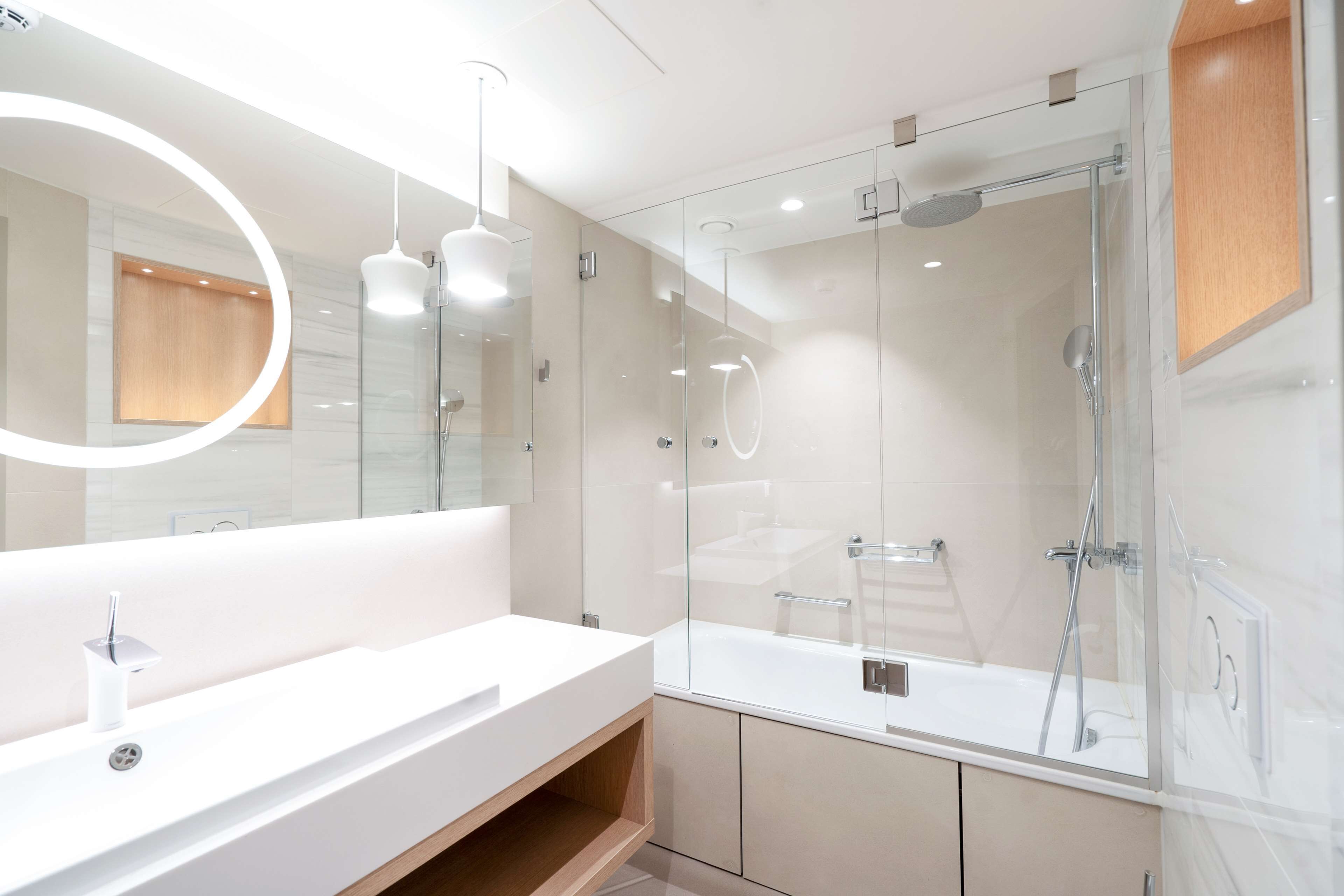 A modern bathroom with a glass-enclosed shower, a white sink, and a large mirror with a circular light.