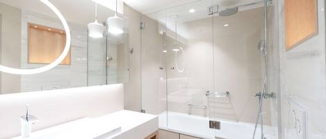 A modern bathroom with a glass-enclosed shower, a white sink, and a large mirror with a circular light.