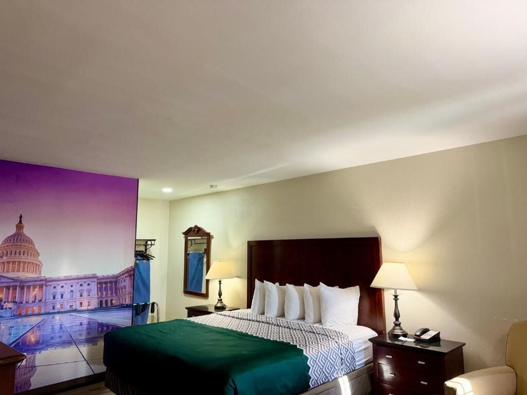 Een hotelkamer met een bed, twee nachtkastjes, een lamp, een stoel en een muurschildering van een gebouw.