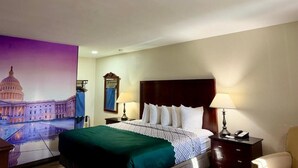 Habitación de hotel con cama, dos mesitas de noche, lámpara, una silla y un mural en la pared que muestra un edificio.