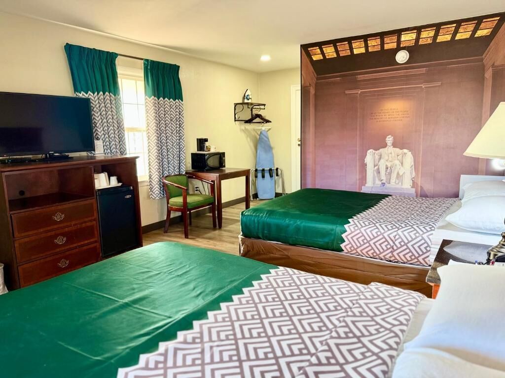Habitación de hotel con dos camas, un televisor, un escritorio con una computadora y una estatua.