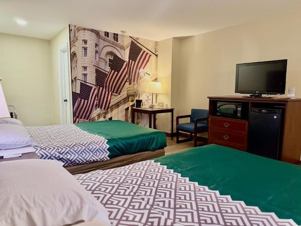 A hotel room with two beds, a desk with a chair, a television, and a refrigerator.