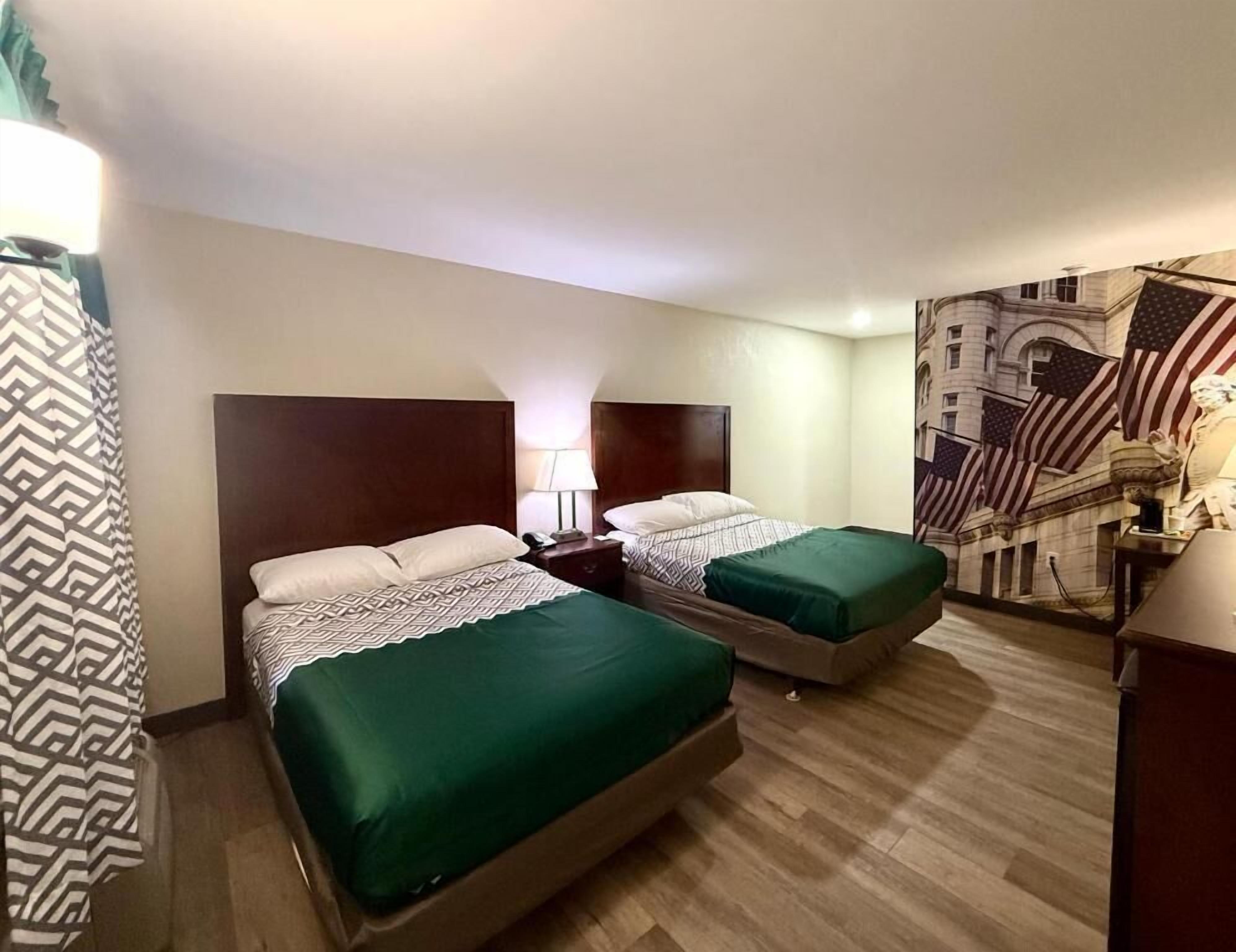 Une chambre d’hôtel avec deux lits, une table de chevet, une lampe et une grande fresque murale représentant le drapeau américain.
