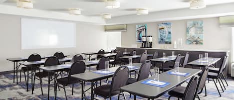 A conference room with tables, chairs, a projector screen, and artwork on the walls.