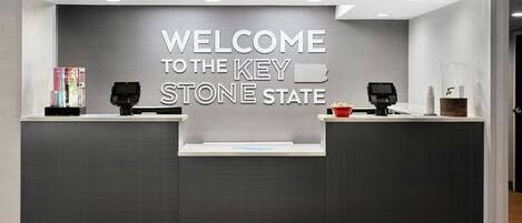A reception desk with a "WELCOME TO THE KEY STONE STATE" sign, two card readers, and a small display stand with a book.