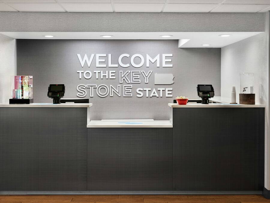 A reception desk with a "WELCOME TO THE KEY STONE STATE" sign, two card readers, and a small display stand with a book.