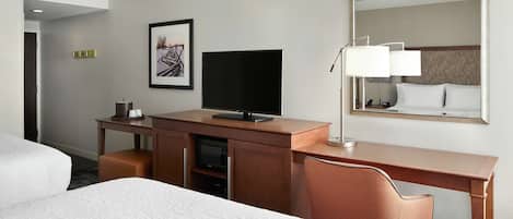Una habitación de hotel con una cama, un escritorio con televisor, una silla y un espejo grande.
